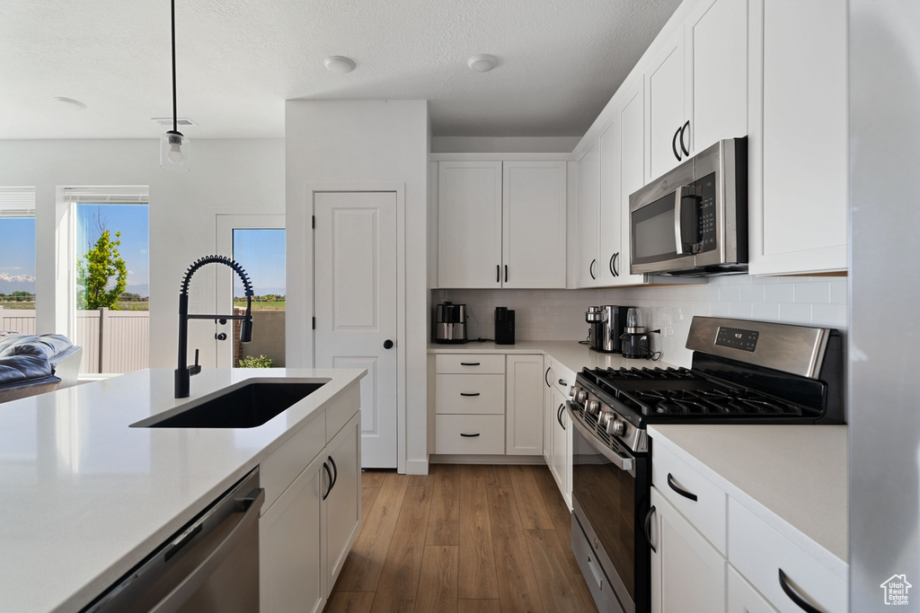 Kitchen with stainless steel appliances, a sink, light countertops, light wood-type flooring, and backsplash