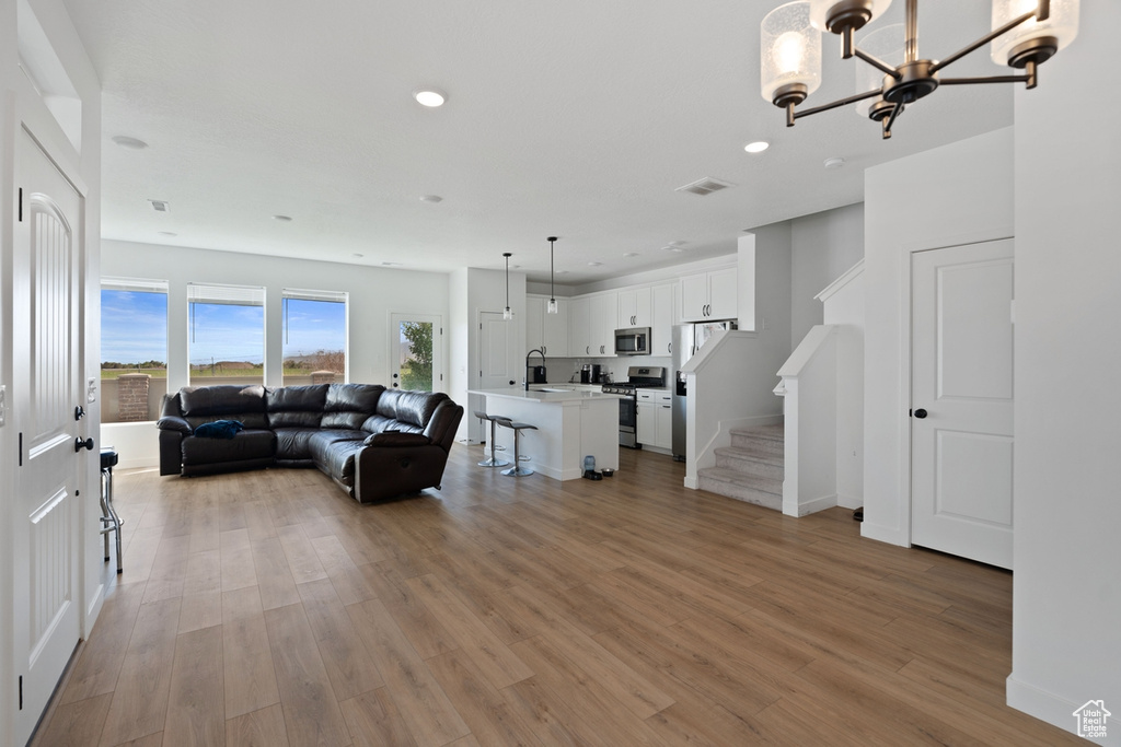 Living room featuring recessed lighting, light wood-type flooring, a chandelier, stairs, and baseboards