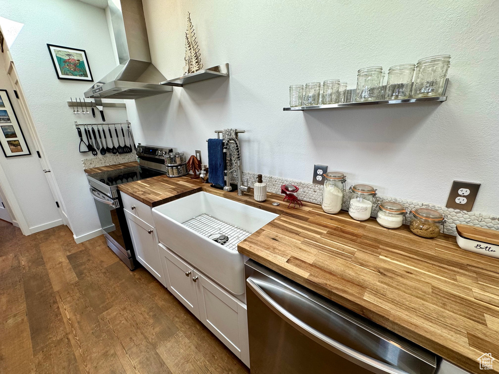 Kitchen with butcher block countertops, appliances with stainless steel finishes, a sink, wall chimney exhaust hood, and dark wood-style floors