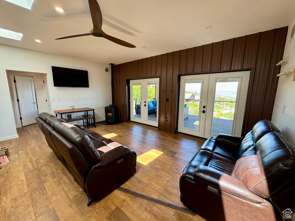 Living area with french doors, plenty of natural light, ceiling fan, light wood-type flooring, and wooden walls