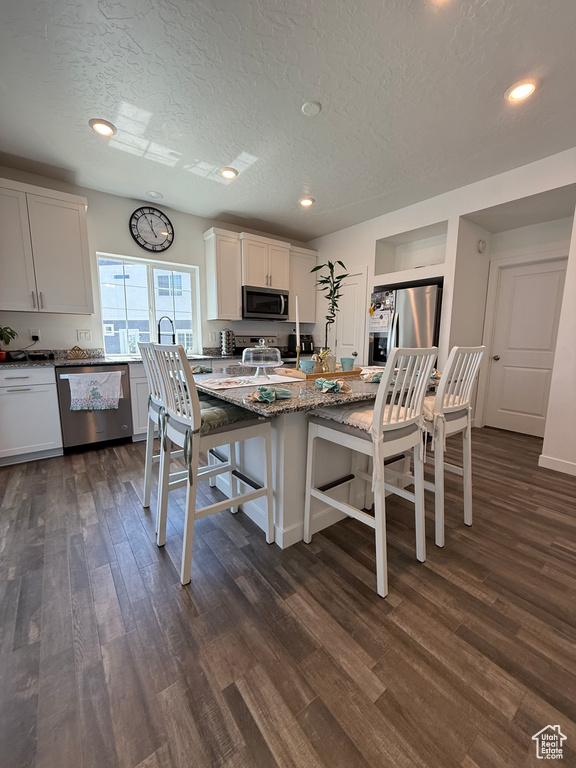 Kitchen with appliances with stainless steel finishes, dark wood-style floors, a kitchen bar, a textured ceiling, and stone countertops