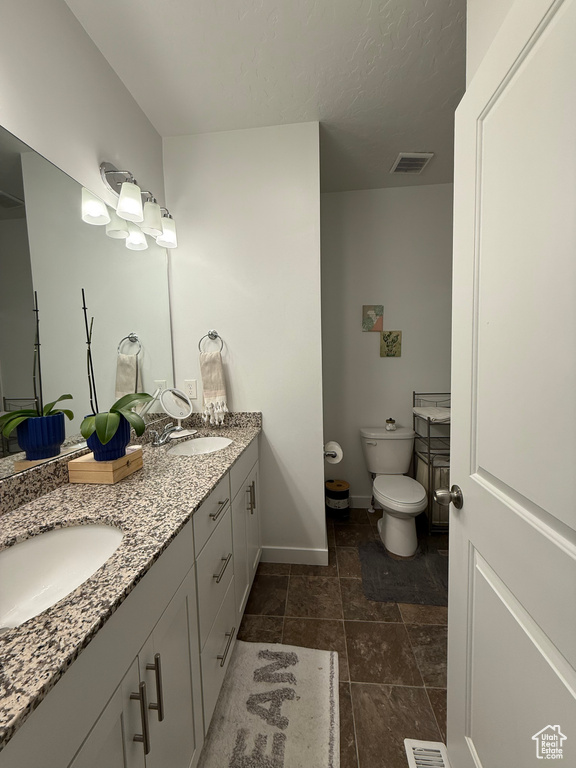Full bathroom with toilet, baseboards, double vanity, and stone finish flooring