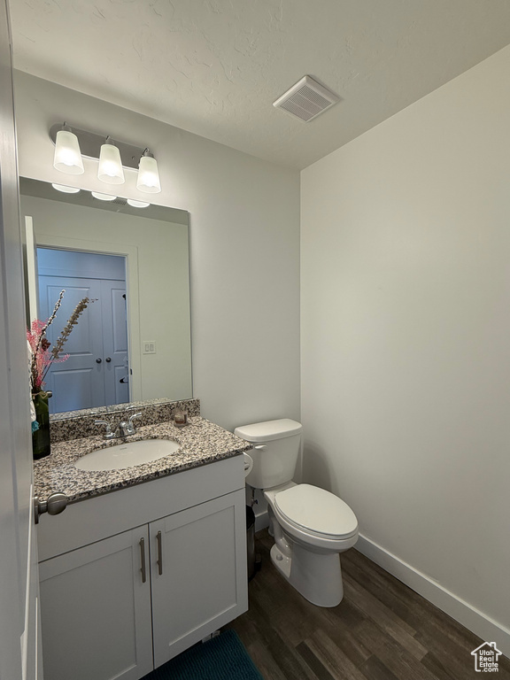 Half bathroom featuring wood finished floors, toilet, baseboards, and vanity