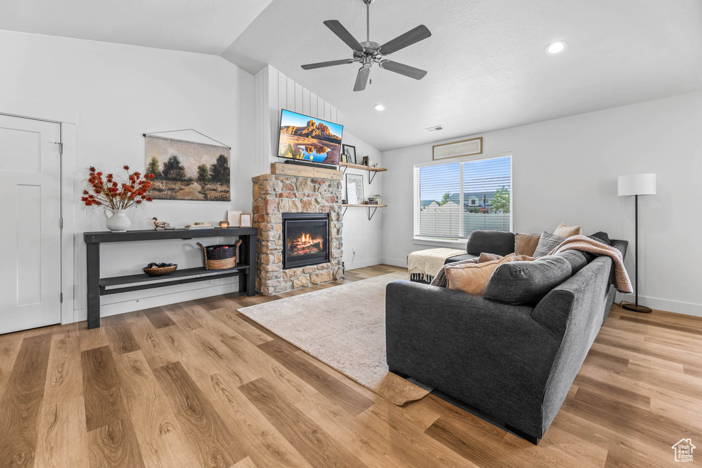Living area with lofted ceiling, a stone fireplace, a ceiling fan, wood finished floors, and recessed lighting