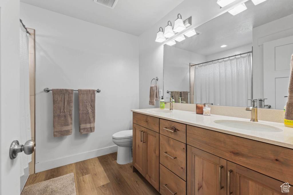 Full bathroom with double vanity, wood finished floors, toilet, baseboards, and curtained shower