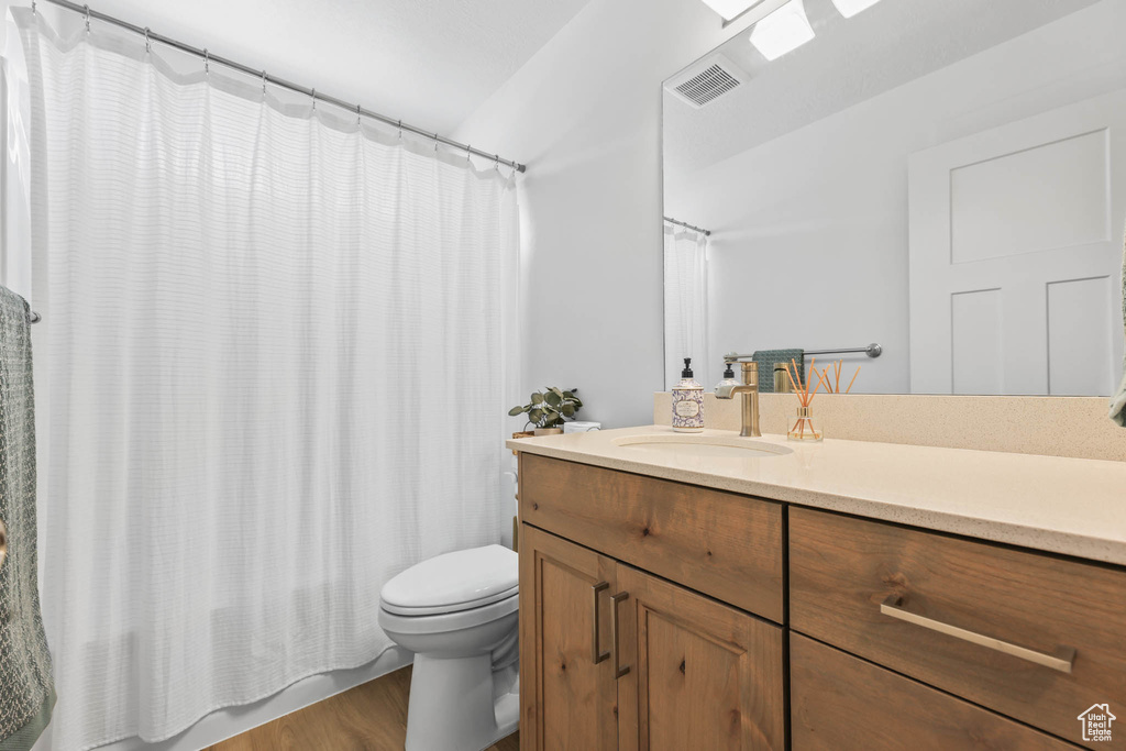 Bathroom with vanity, toilet, wood finished floors, and shower / bath combo with shower curtain