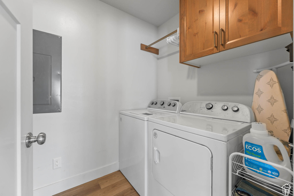 Laundry room featuring cabinet space, electric panel, separate washer and dryer, light wood-style flooring, and baseboards