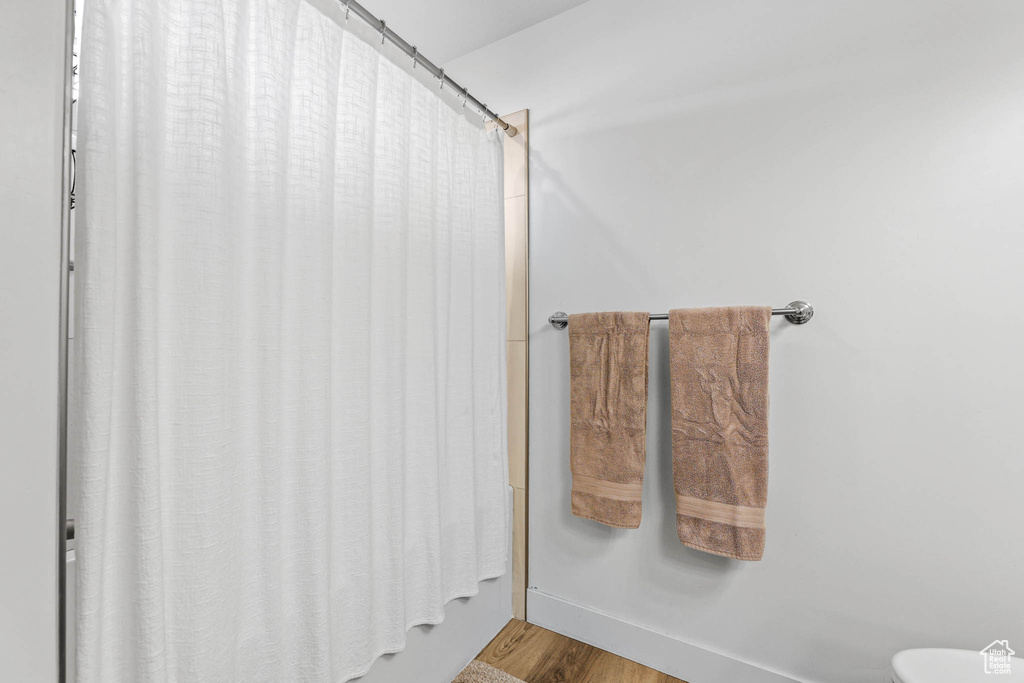 Bathroom with toilet, wood finished floors, and a shower with shower curtain
