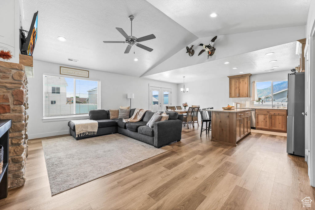 Living area with ceiling fan, vaulted ceiling, light wood-style floors, healthy amount of natural light, and a fireplace