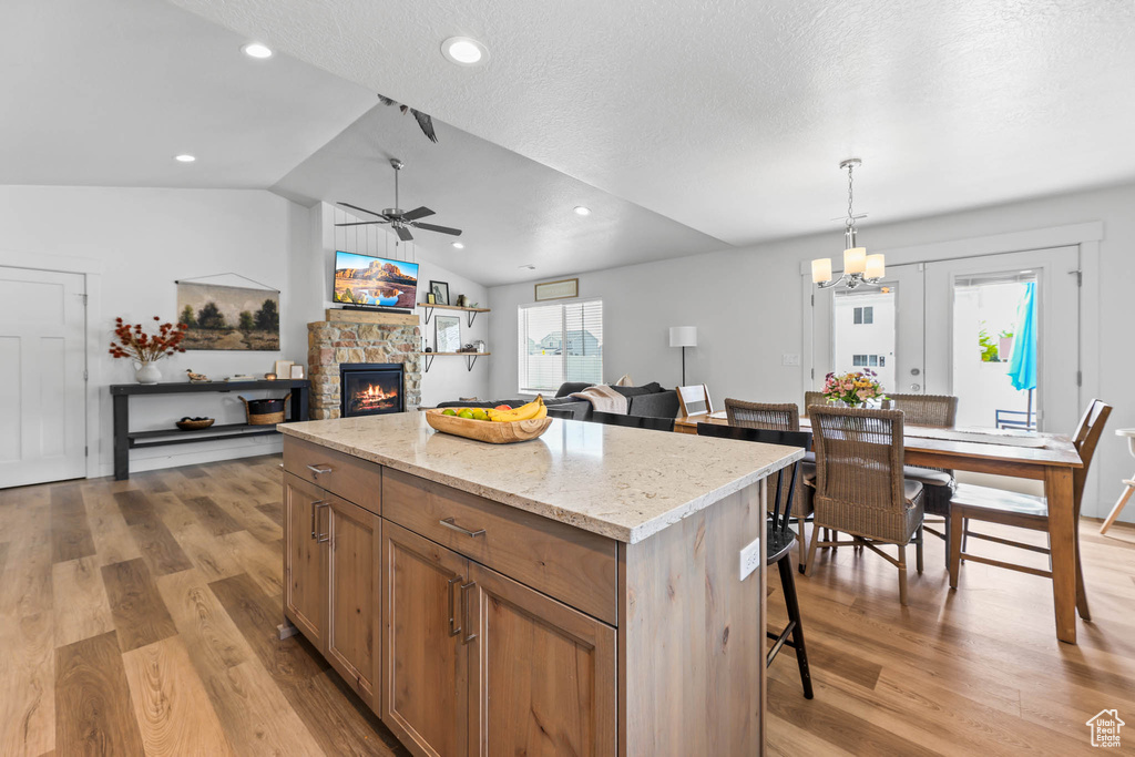 Kitchen featuring a ceiling fan, a kitchen island, light wood-type flooring, a stone fireplace, and lofted ceiling