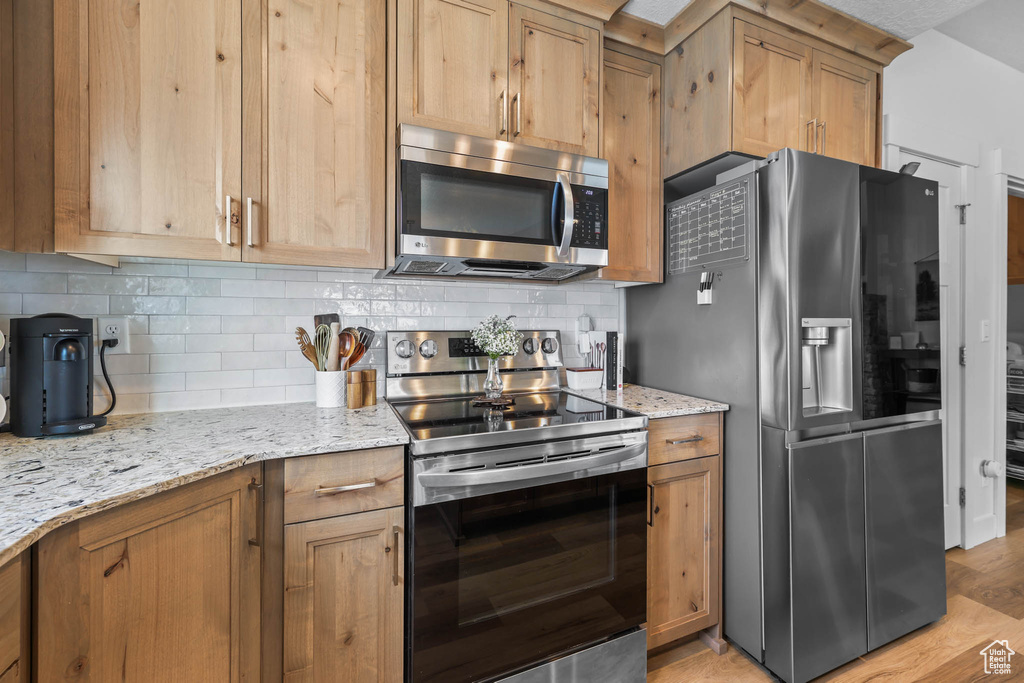 Kitchen featuring appliances with stainless steel finishes, tasteful backsplash, light stone counters, and light wood-type flooring