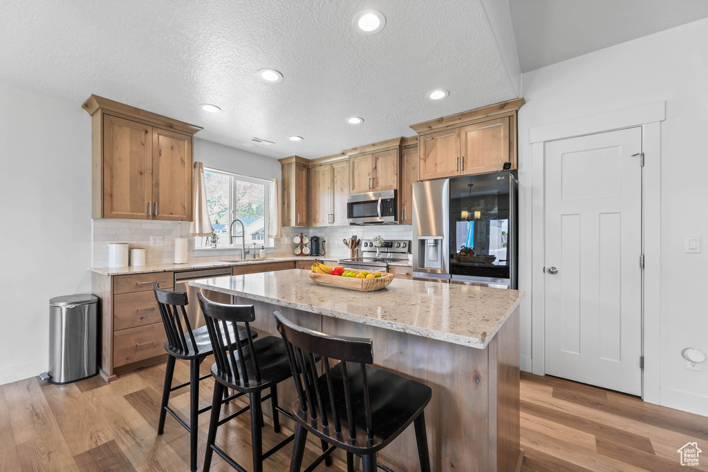 Kitchen with appliances with stainless steel finishes, a sink, decorative backsplash, light wood-type flooring, and recessed lighting