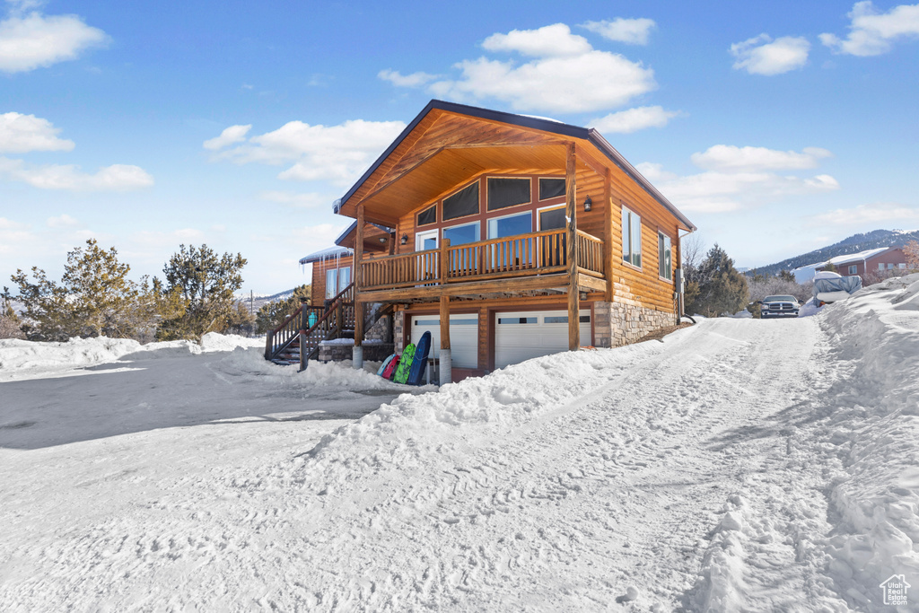 Snow covered property with stairway, a garage, and stone siding