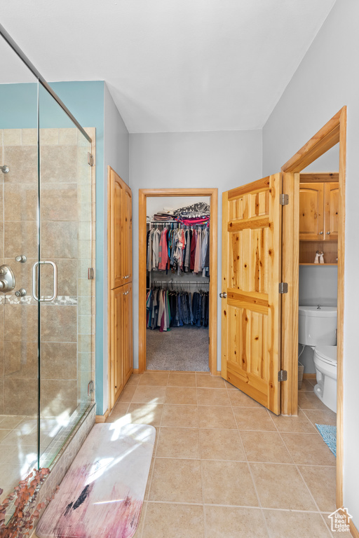 Bathroom with toilet, tile patterned floors, a shower stall, and a spacious closet