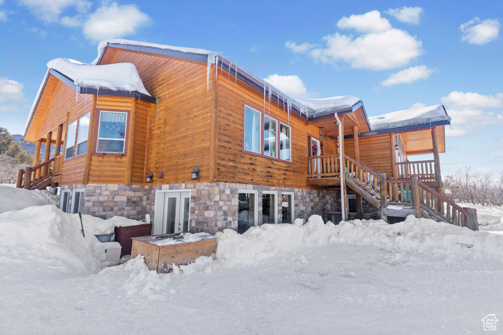 Snow covered property featuring stairs and stone siding