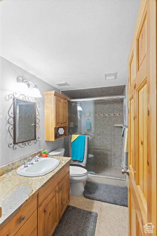 Full bathroom with toilet, vanity, a stall shower, a textured ceiling, and speckled floor