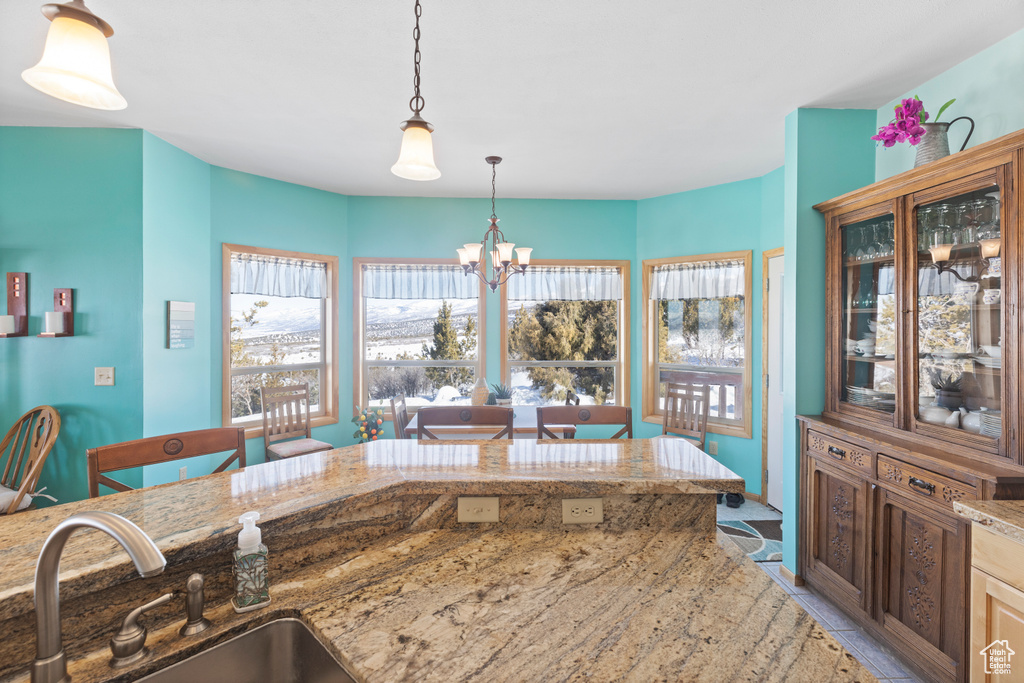 Kitchen featuring a sink, a chandelier, decorative light fixtures, light stone counters, and glass insert cabinets