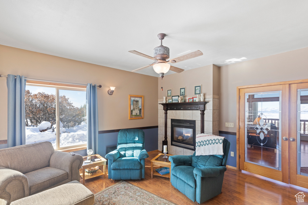 Living area featuring wood finished floors, a tiled fireplace, a ceiling fan, and french doors