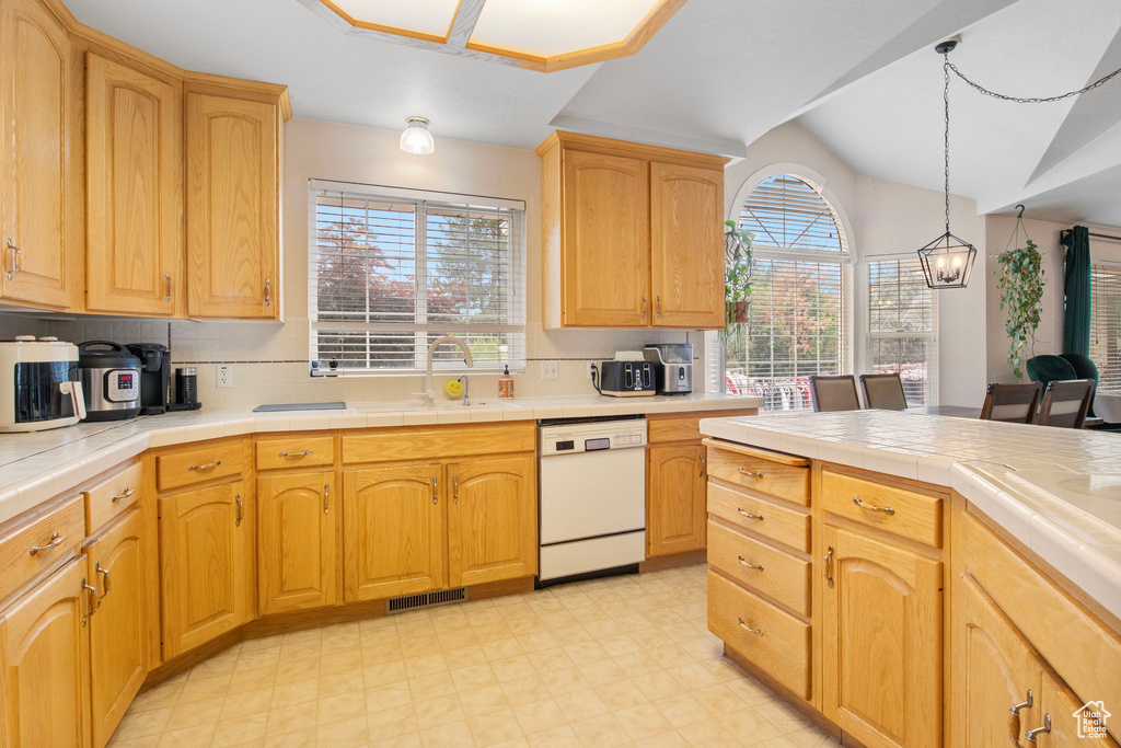 Kitchen with white dishwasher, a sink, tile counters, decorative backsplash, and light flooring