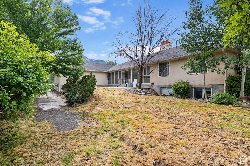 Back of property featuring stucco siding, a chimney, a sunroom, and a yard