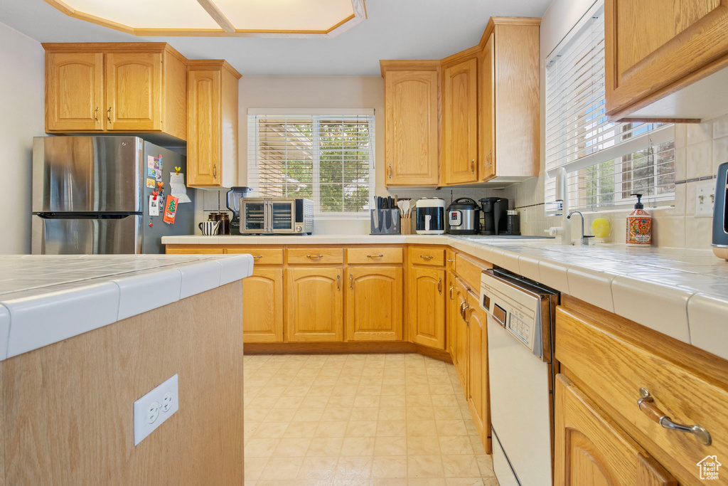Kitchen with freestanding refrigerator, dishwasher, tile countertops, and plenty of natural light