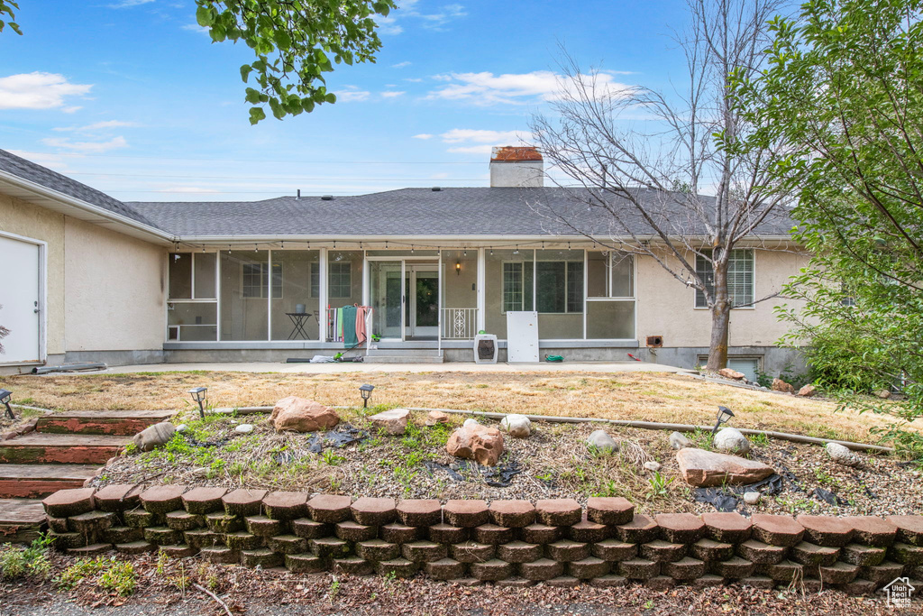 Back of house with stucco siding, a chimney, a shingled roof, and a sunroom