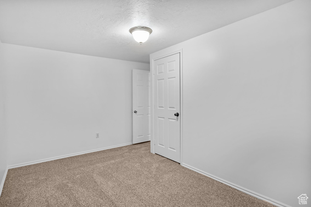 Unfurnished room with light colored carpet, a textured ceiling, and baseboards