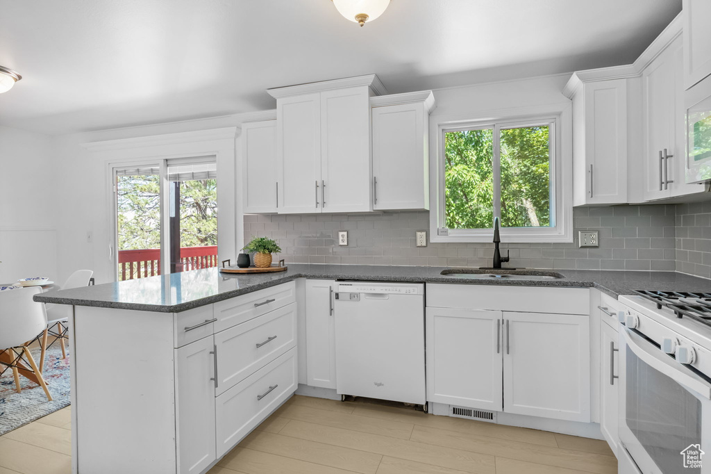 Kitchen featuring white appliances, a sink, tasteful backsplash, a peninsula, and white cabinetry