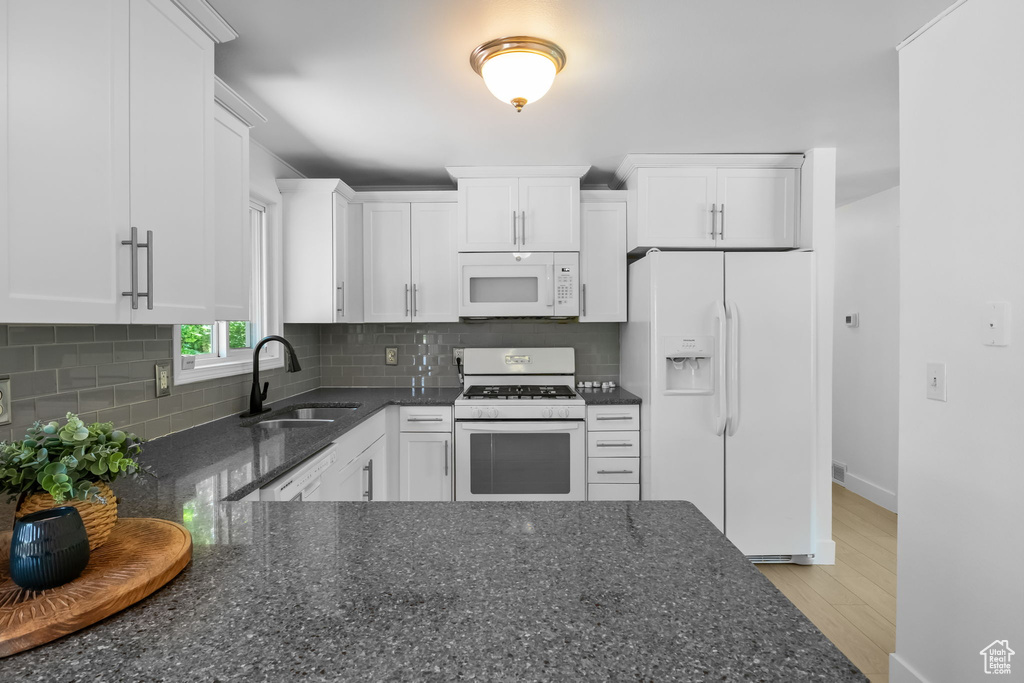 Kitchen with white appliances, a sink, white cabinets, dark stone counters, and tasteful backsplash
