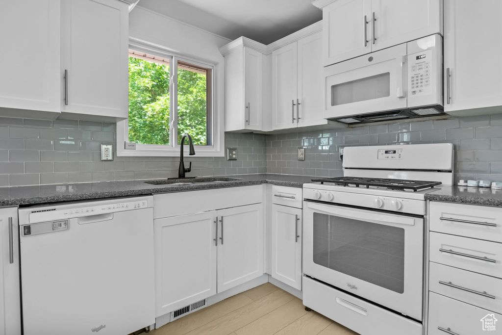 Kitchen with white appliances, a sink, white cabinets, dark stone countertops, and decorative backsplash