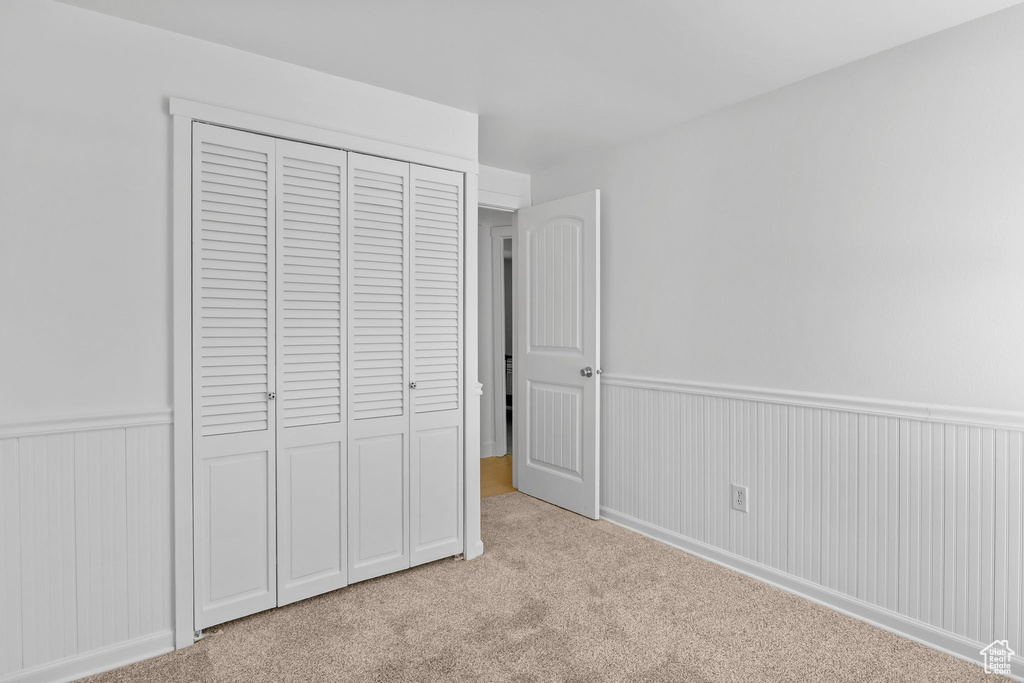 Unfurnished bedroom with wainscoting, light colored carpet, and a closet