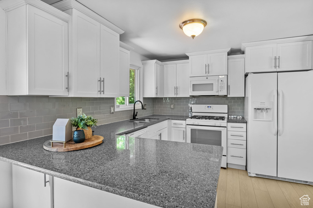 Kitchen featuring white appliances, a sink, a peninsula, and white cabinets