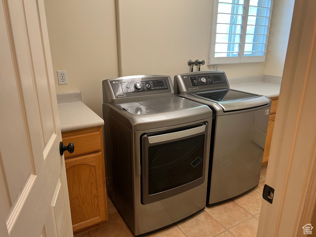 Laundry room featuring washer and clothes dryer, light tile patterned flooring, and cabinet space