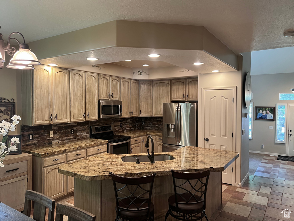 Kitchen featuring appliances with stainless steel finishes, a sink, tasteful backsplash, stone tile floors, and a breakfast bar area