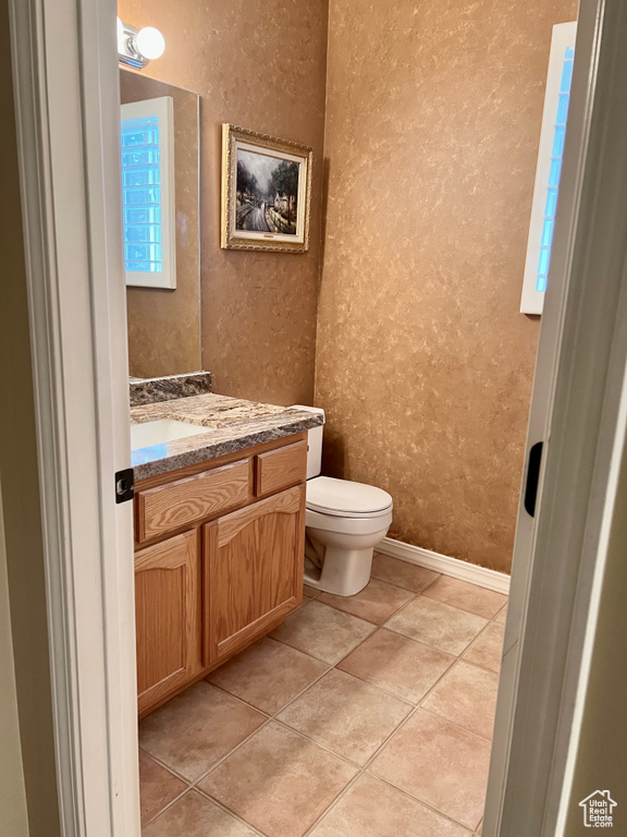 Half bath with a textured wall, vanity, toilet, baseboards, and tile patterned flooring