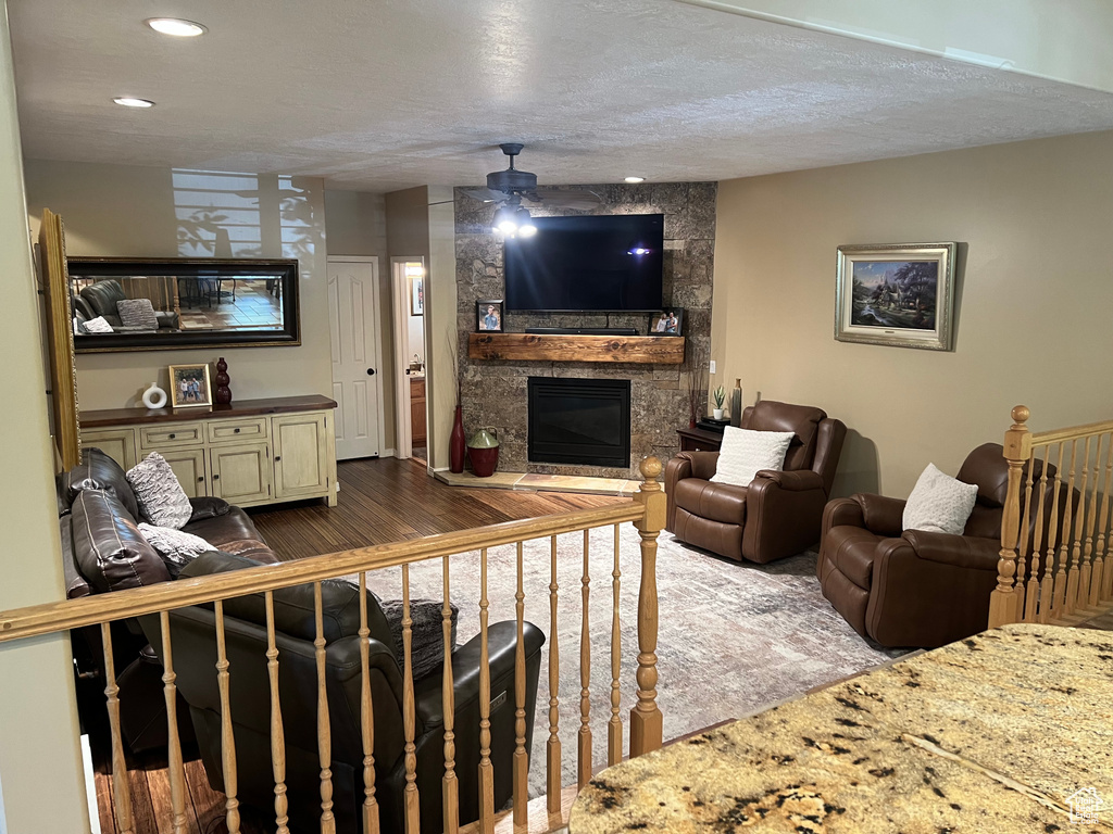 Living area featuring a ceiling fan, a fireplace, dark wood-style flooring, recessed lighting, and a textured ceiling