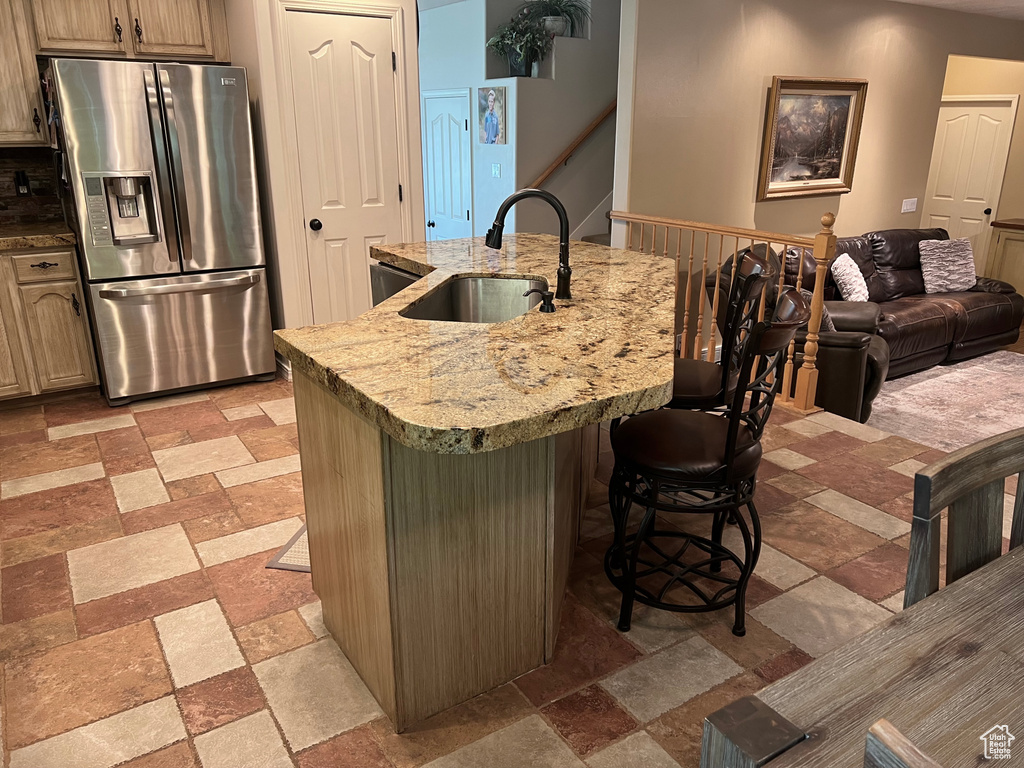 Kitchen with stainless steel fridge, a sink, stone tile flooring, a kitchen bar, and a center island with sink