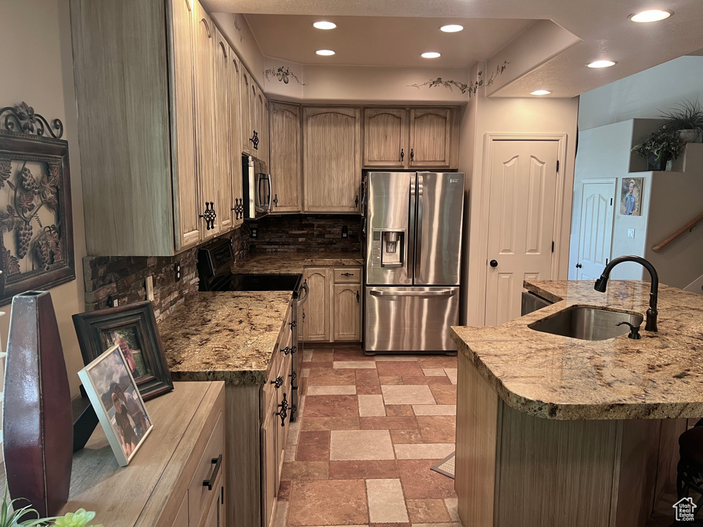Kitchen with appliances with stainless steel finishes, a sink, decorative backsplash, recessed lighting, and light stone counters