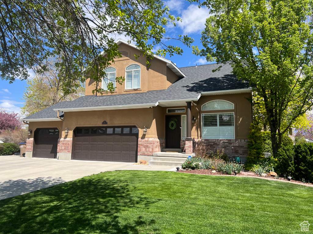 View of front of home with stucco siding, a front yard, an attached garage, concrete driveway, and stone siding