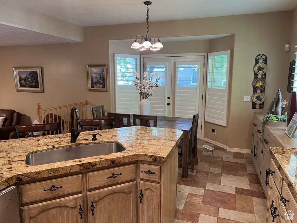 Kitchen featuring a sink, stone tile floors, decorative light fixtures, baseboards, and light stone countertops