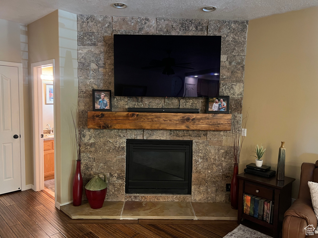Detailed view of wood finished floors, a stone fireplace, a textured ceiling, and baseboards