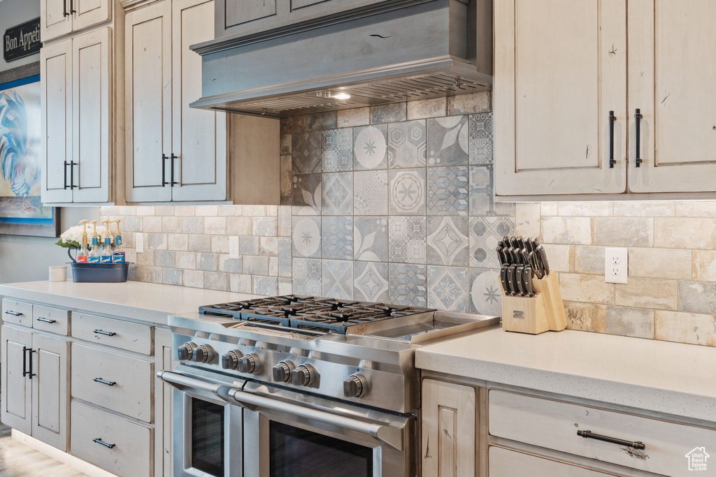 Kitchen featuring high end stove, ventilation hood, light countertops, and backsplash