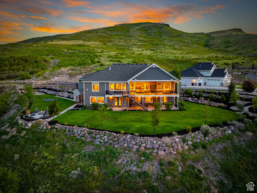 Back of property at dusk with stairs, a yard, a mountain view, and a balcony