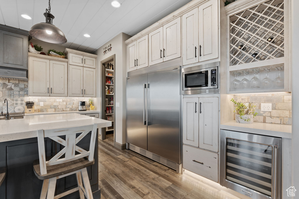Kitchen featuring built in appliances, wine cooler, recessed lighting, backsplash, and a sink