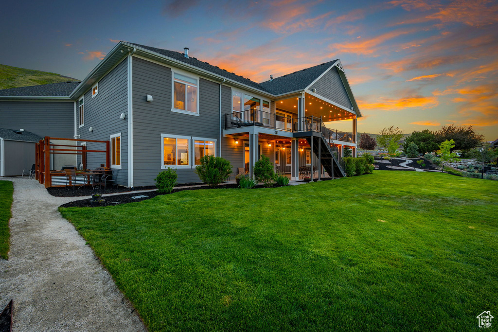 Back of house at dusk featuring a deck, a lawn, and stairs