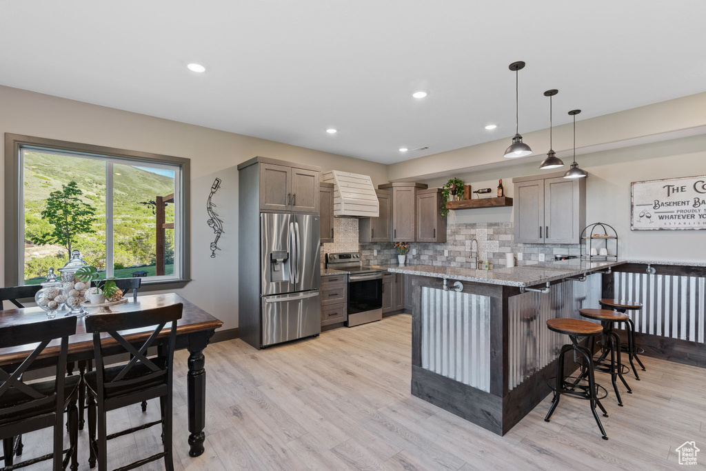 Kitchen featuring appliances with stainless steel finishes, open shelves, a sink, light stone counters, and a breakfast bar area