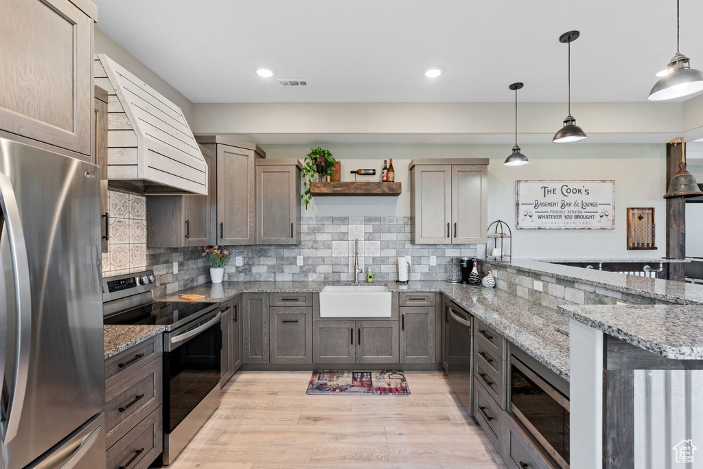 Kitchen with stainless steel appliances, a sink, a peninsula, open shelves, and custom exhaust hood