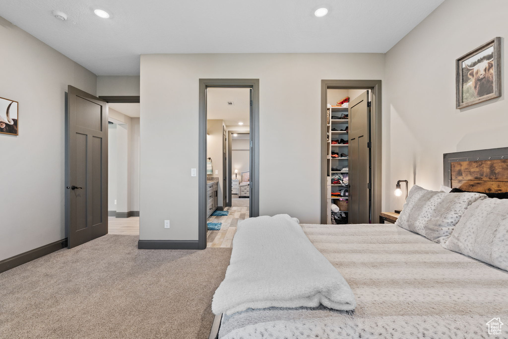 Bedroom with a spacious closet, light carpet, recessed lighting, baseboards, and ensuite bath