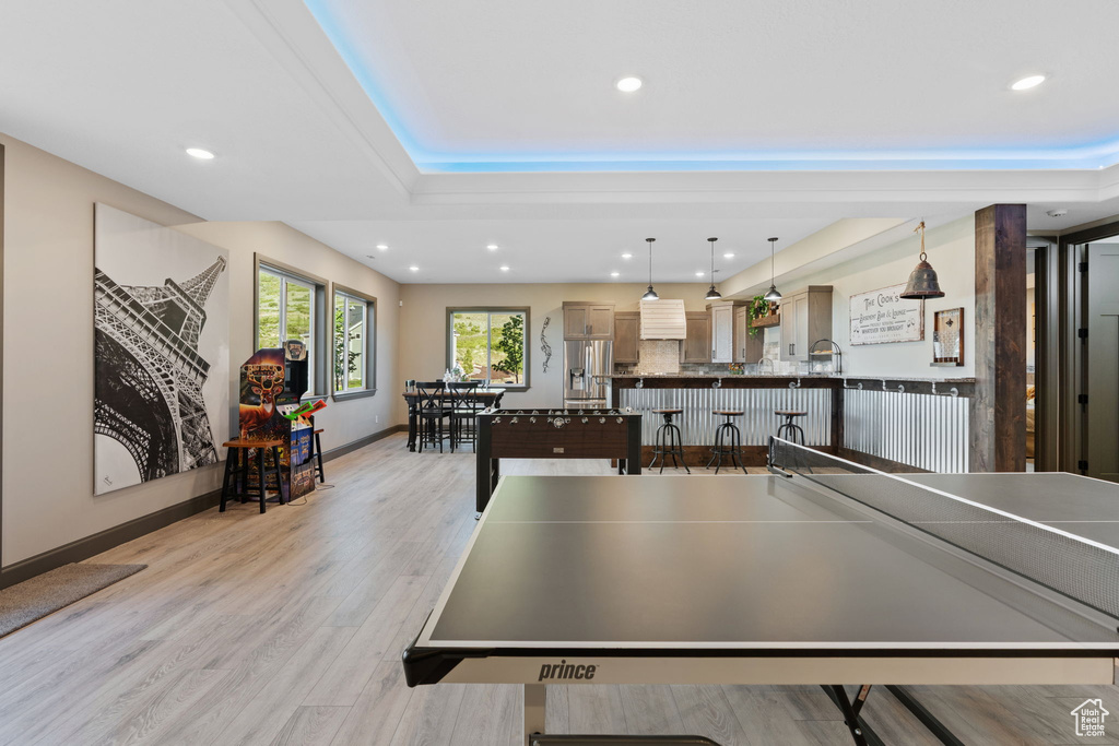 Game room featuring light wood-style flooring, a raised ceiling, recessed lighting, and baseboards