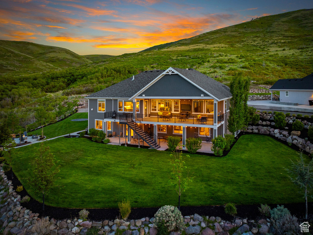 Back of property at dusk with a patio, stairway, a deck with mountain view, and a lawn